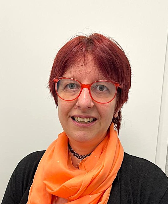 Frau mit roten Haaren und Brille lächelt freundlich und trägt einen orangen Schal
